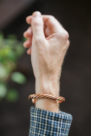 Kopero Kupferarmband Gedreht, am Handgelenk, mit der Hand nach oben vor einem dunklen Hintergrund