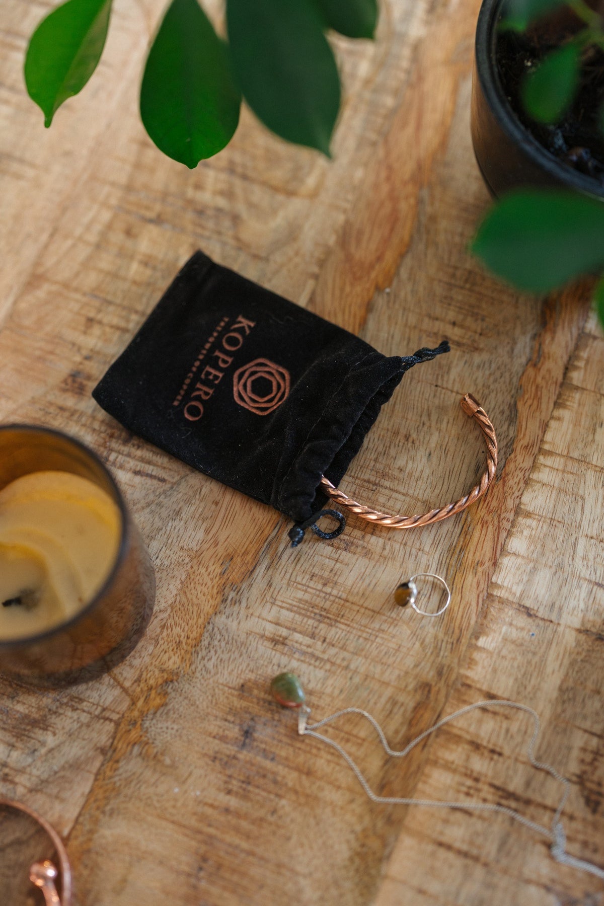Kopero Kupferarmband Gedreht, auf einem Holztisch neben dem Samtbeutel, einer Kerze und Schmuck