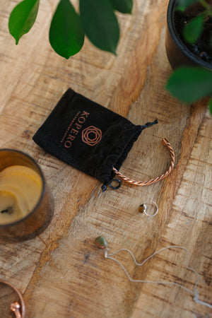 Kopero Kupferarmband Gedreht, auf einem Holztisch neben dem Samtbeutel, einer Kerze und Schmuck