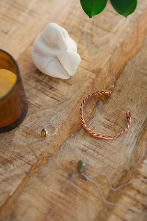Kopero Kupferarmband Gedreht, auf einem Holztisch neben einer Figur und einem Ring