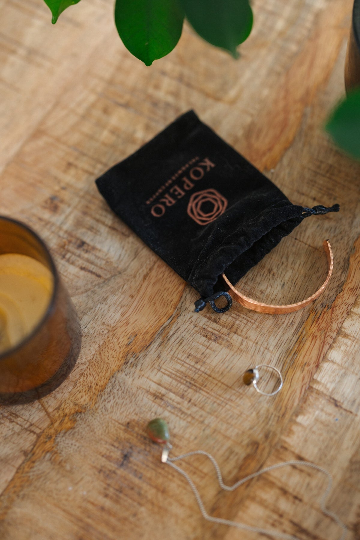 Kopero Kupferarmband Gehämmert, auf einem Holztisch neben dem Samtbeutel, einer Kerze und Schmuck
