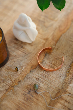 Kopero Kupferarmband Gehämmert, auf einem Holztisch neben einer Figur und einem Ring