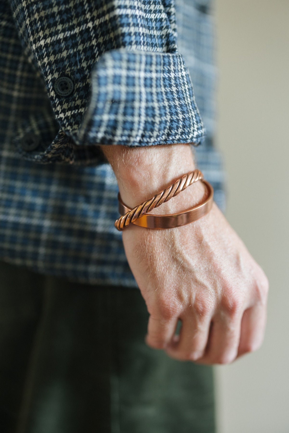 Kopero Kupferarmband Glatt, am Handgelenk über einem karierten Hemdärmel, zusammen mit einem gedrehten Armband