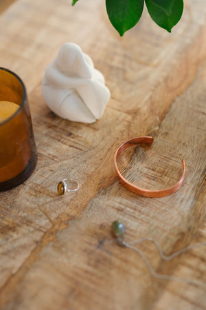 Kopero Kupferarmband Glatt, auf einem Holztisch neben einer Figur und einem Ring