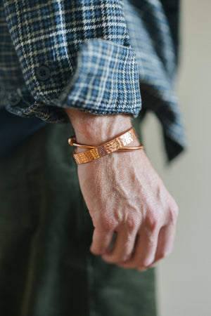 Kopero Kupferarmband Rund, am Handgelenk über einem karierten Hemdärmel, zusammen mit einem gehämmerten Armband