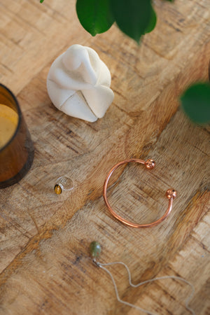 Kopero Kupferarmband Rund, auf einem Holztisch neben einer Figur und einem Ring