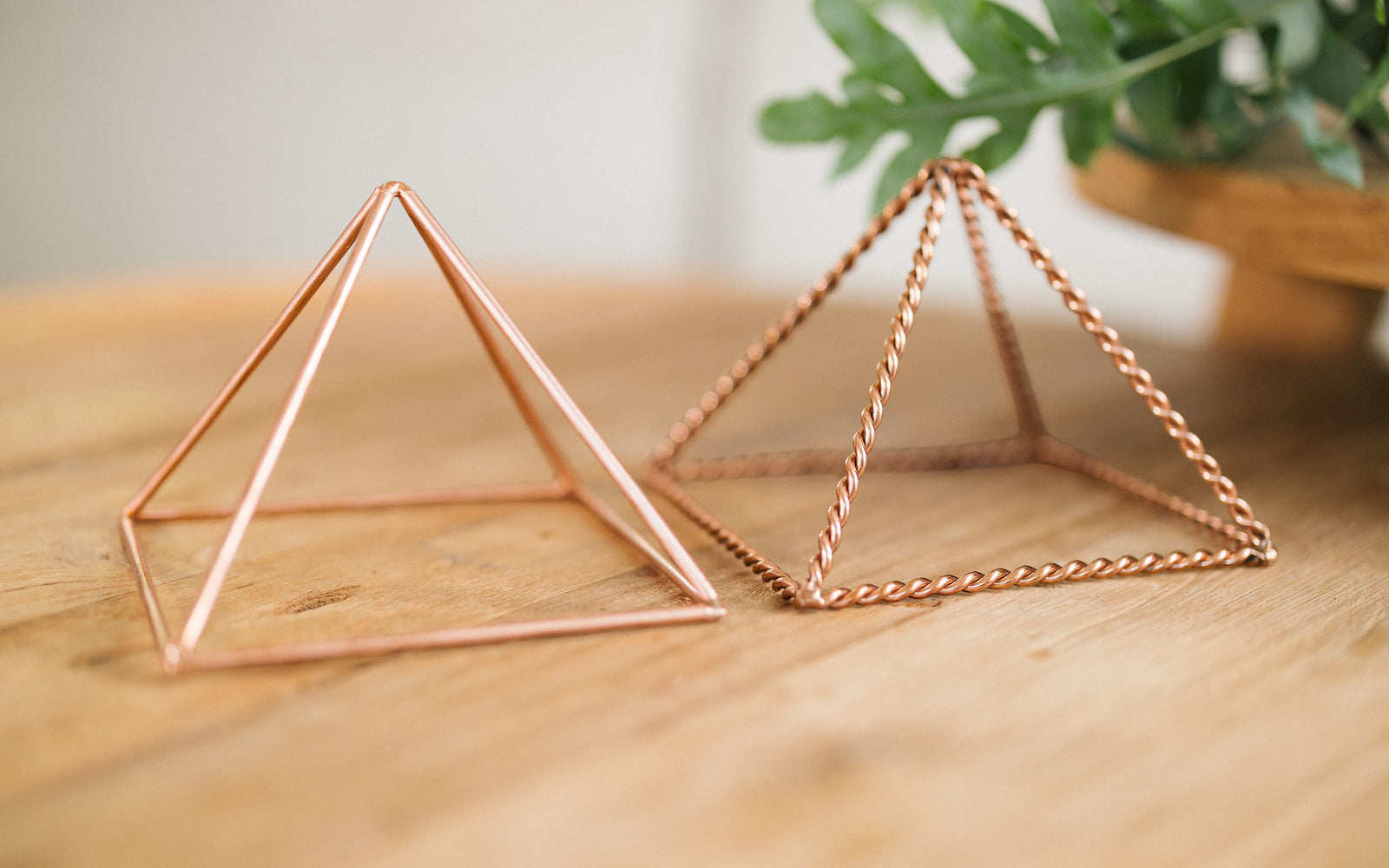 Zwei Kupferpyramiden, gedreht und glatt, nebeneinander auf einem Holztisch