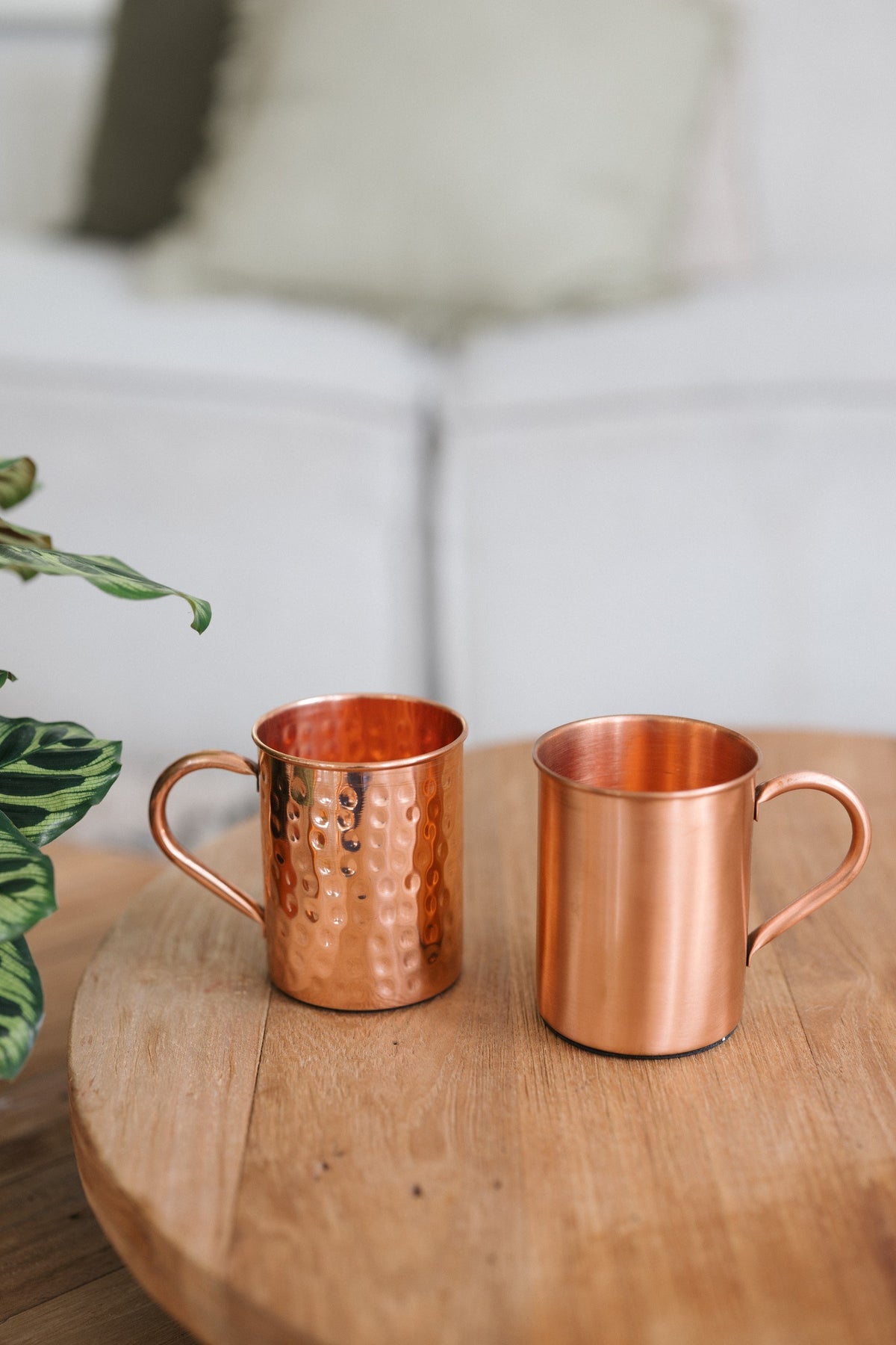 Kopero Kupfertasse, eine glatte und eine gehämmerte Tasse nebeneinander auf einem runden Holztisch