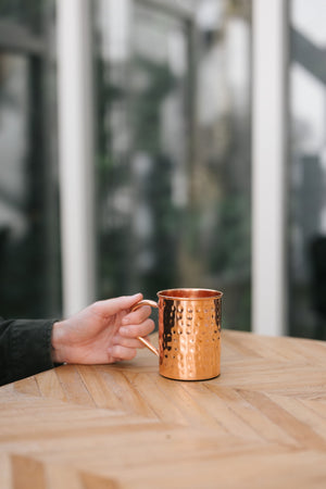 Kopero Kupfertasse Gehämmert, auf einem Holztisch, mit einer Hand am Henkel