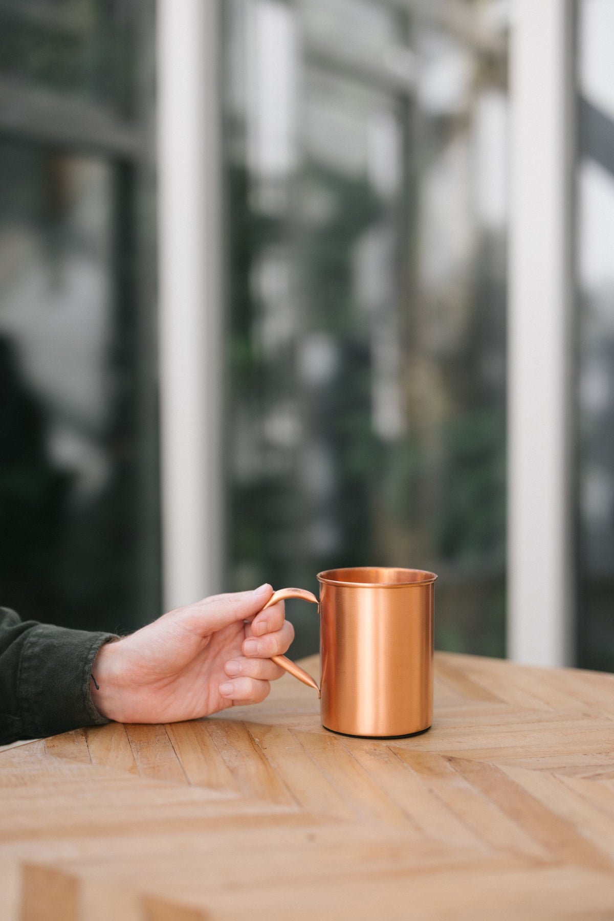 Kopero Kupfertasse Glatt, auf einem Holztisch, mit einer Hand am Henkel