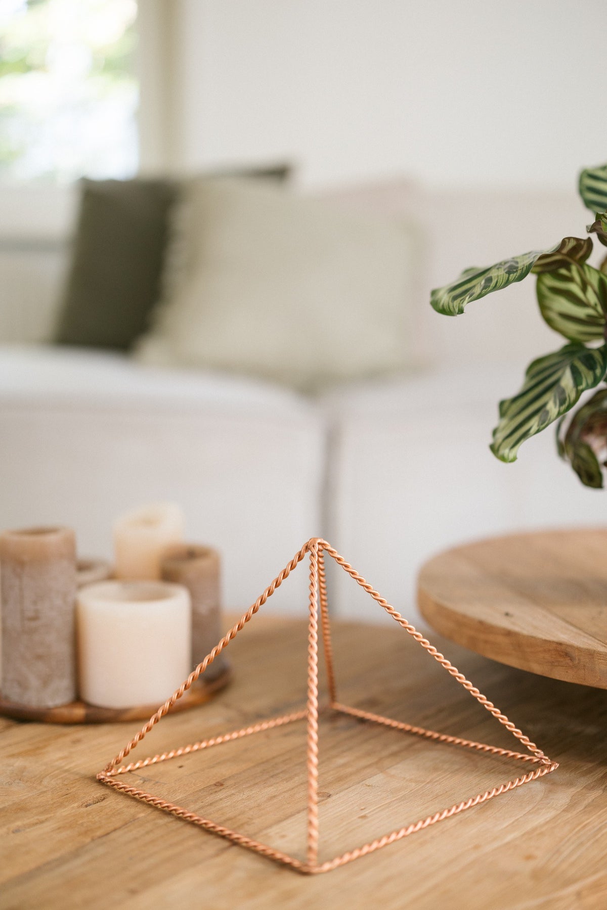 Kopero Kupfer-Pyramide Energizer Gedreht Groß (23,56 cm), auf einem hölzernen Couchtisch vor einem Sofa, neben Kerzen