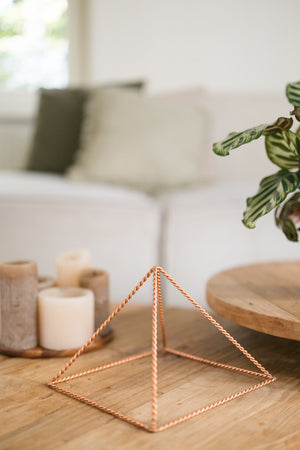 Kopero Kupfer-Pyramide Energizer Gedreht Groß (23,56 cm), auf einem hölzernen Couchtisch vor einem Sofa, neben Kerzen