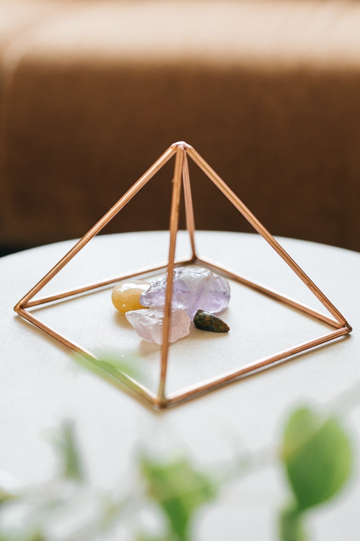 Kopero Kupfer-Pyramide Energizer Glatt Klein (14,56 cm), mit Edelsteinen darunter auf einem weißen Tischchen