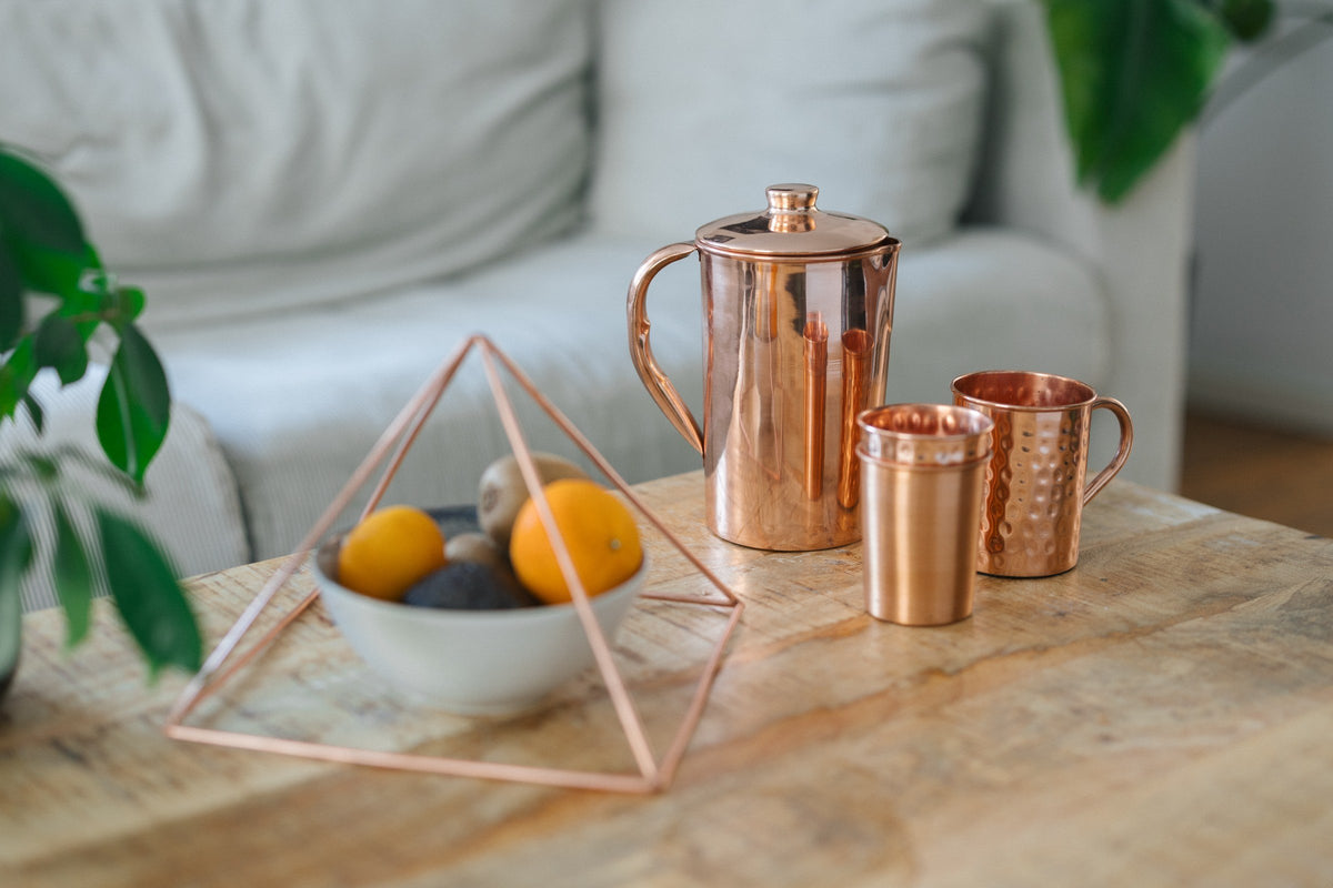 Kupferpyramide über einer Obstschale, daneben eine Kanne, ein Becher und eine Tasse auf einem Holztisch