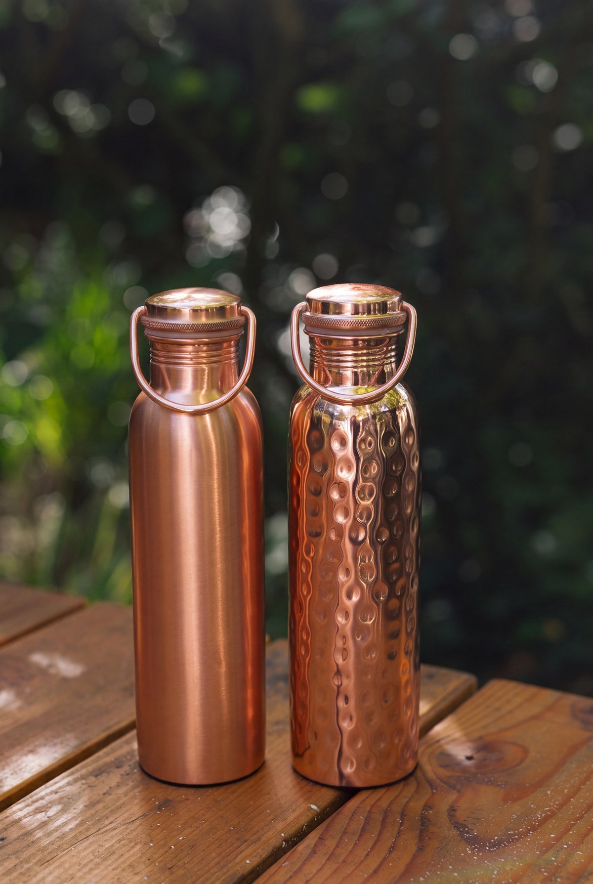 Kopero Kupferflasche, die glatte und die gehämmerte Flasche nebeneinander auf einem Holztisch im Garten