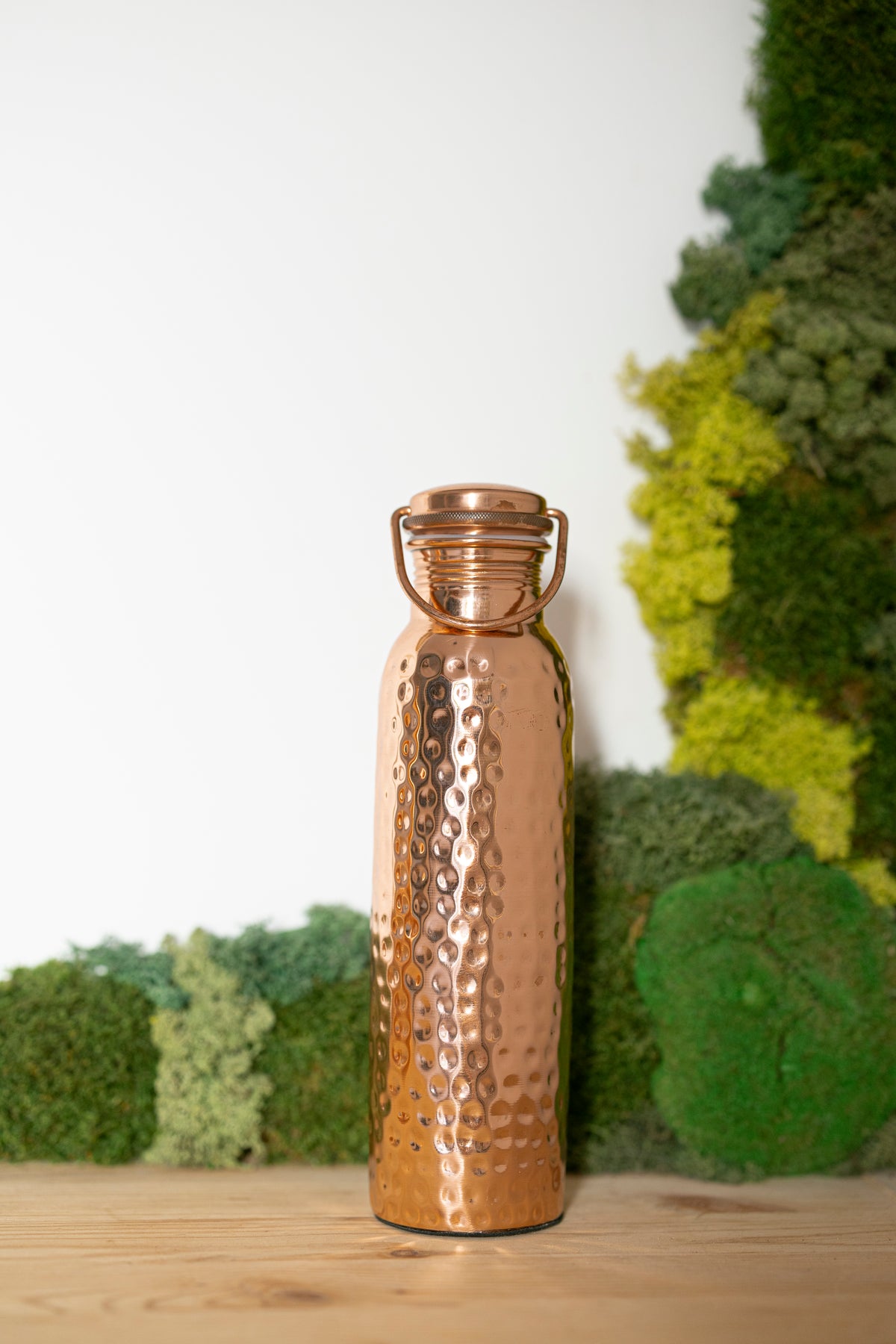 Kopero Kupfer-Wasserflasche Gehämmert, 900 ml, aufrecht auf einem Holztisch vor einem Moosgrund