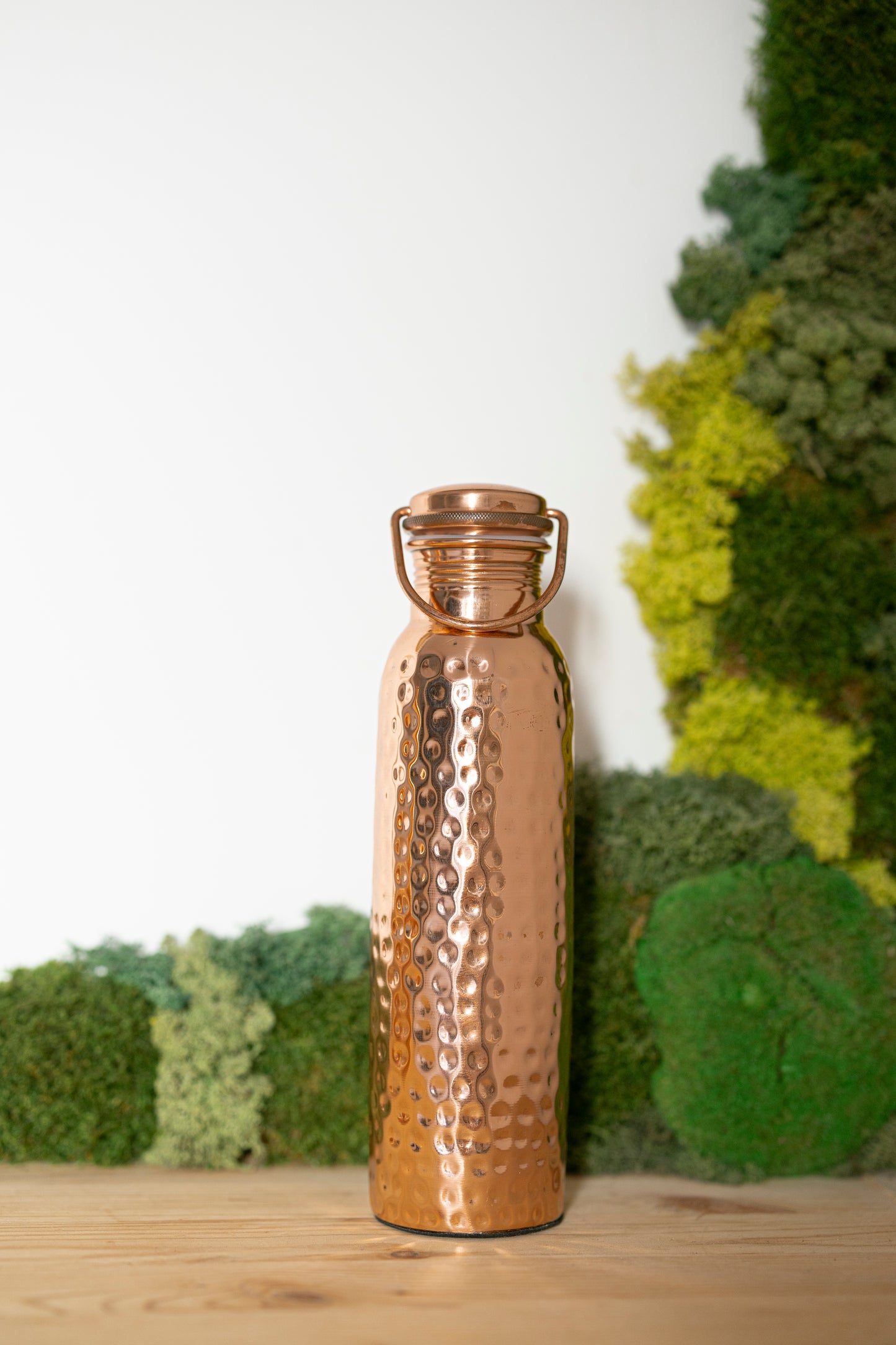 Kopero Kupfer-Wasserflasche Gehämmert, 900 ml, aufrecht auf einem Holztisch vor einem Moosgrund
