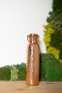 Kopero Kupfer-Wasserflasche Gehämmert, 900 ml, aufrecht auf einem Holztisch vor einem Moosgrund
