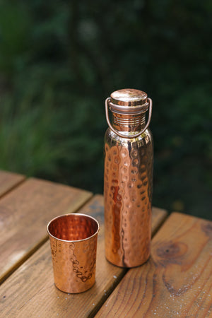 Kopero Kupferflasche Gehämmert, auf einem Holztisch im Garten neben einem gehämmerten Becher