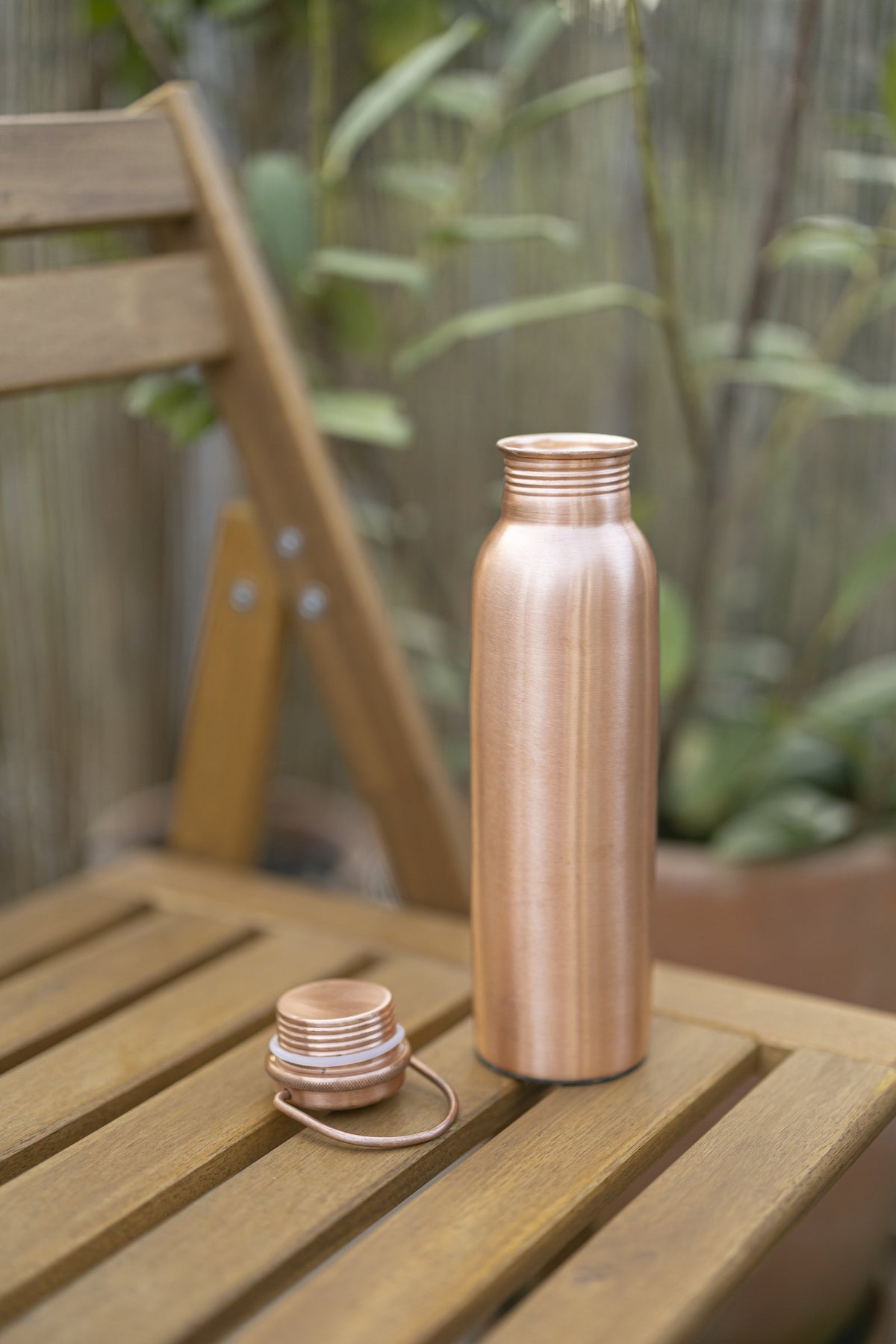 Kopero Kupferflasche Glatt auf einem Holzgartenstuhl, mit dem Deckel daneben