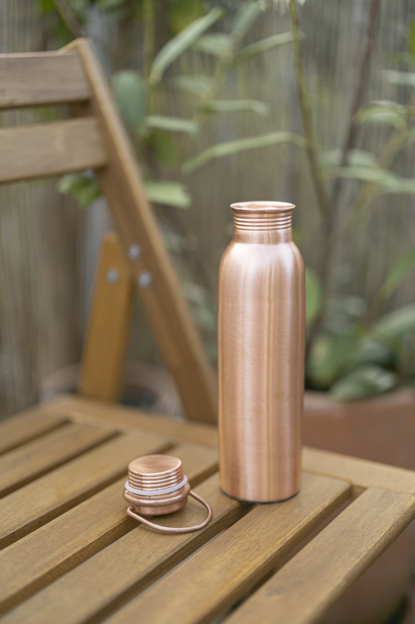 Kopero Kupferflasche Glatt auf einem Holzgartenstuhl, mit dem Deckel daneben
