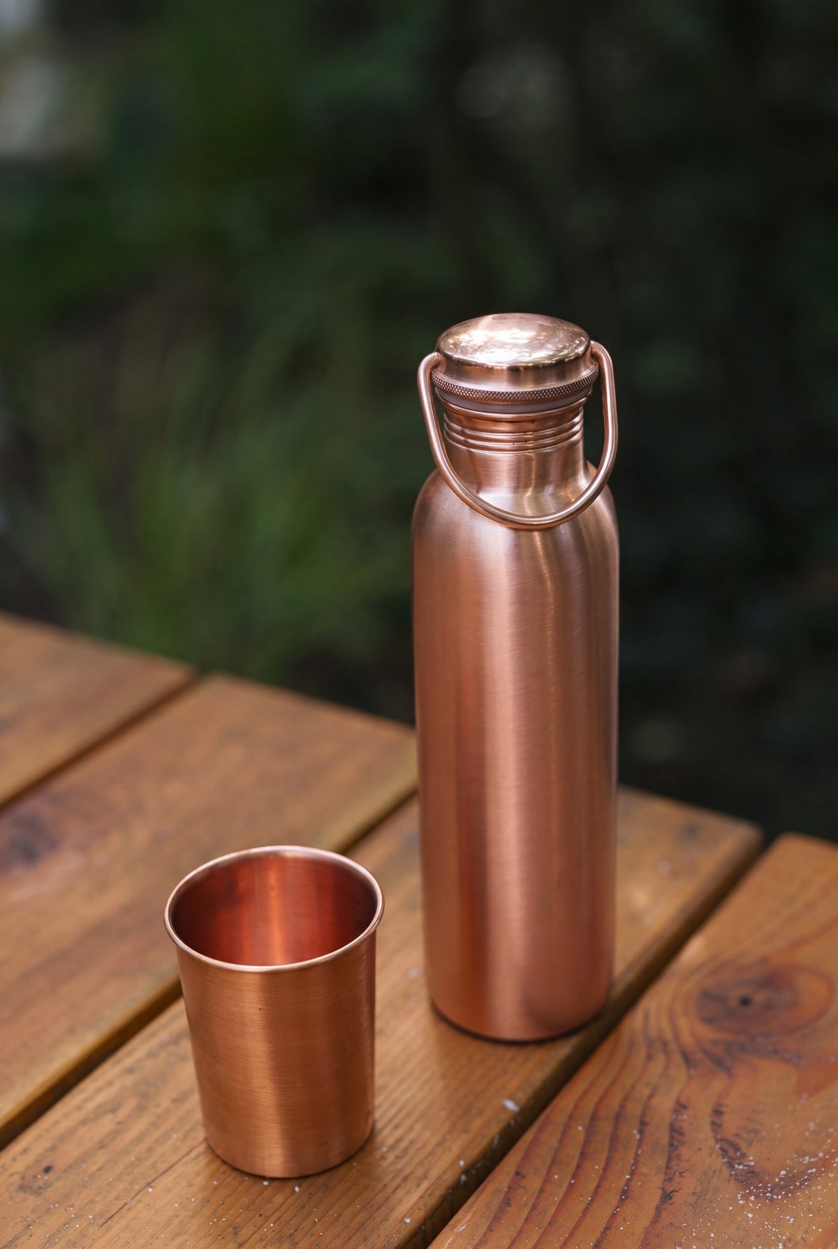Kopero Kupferflasche Glatt, auf einem Holztisch im Garten neben einem kupfernen Becher